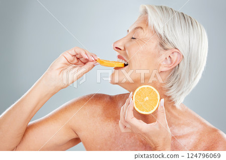 Beauty, orange and eating with a mature woman biting into a fruit slice in studio on a gray background. Food, wellness and natural care with a senior female posing to promote healthy eating or diet 124796069