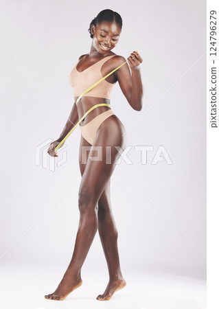 Fitness, lingerie and black woman with measuring tape in studio for weight loss, detox and diet against white background. Body, model and slimming goals by girl happy with results, stomach and weight 124796279