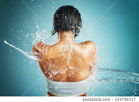 Water splash, shower and woman in studio for wellness, cleaning and body, grooming and back on blue background. Beauty splash, hair and girl model in water for washing, skincare and beauty hygiene 124796317