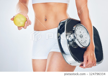 Woman, scale and apple for diet, weightloss or health with fitness, closeup or nutrition by grey background. Model, girl and stomach with fruit, food or balance for goal, vision or wellness in studio 124796334