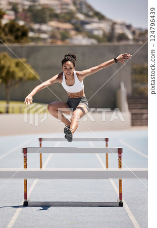 Fitness, training and woman jumping hurdles for sports, exercise and intense cardio on a running track. Black woman, running and hurdling workout for speed, energy and physical performance at stadium 124796439