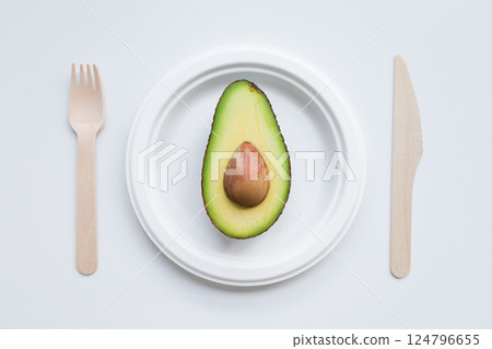 Minimalist composition with avocado halve on white plate and wooden cutlery 124796655