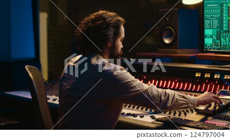 Portrait of music producer working in control room professional studio and editing audio recordings, mixing console and daw software in soundproof space. Sound engineer in post production. Camera A. Portrait of music producer working in control room professional studio and editing audio recordings, mixing console and daw software in soundproof space. Sound engineer in post production. Camera A. 124797004