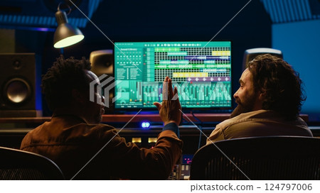 Pleased artist and tracking engineer doing high five gesture after creating a song together, happy with the final result. Team of singer and producer celebrating successful track collab. Camera A. Pleased artist and tracking engineer doing high five gesture after creating a song together, happy with the final result. Team of singer and producer celebrating successful track collab. Camera A. 124797006