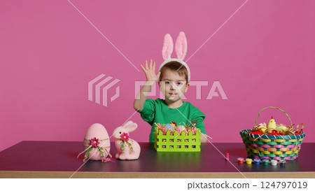 Excited little kid decorating baskets with eggs and grass to prepare for easter holiday festivity, creating festive arrangements. Cute toddler with bunny ears does craft activity. Camera B. 124797019