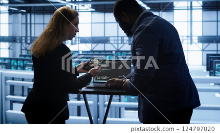 Team of developers doing maintenance checkup using laptop to prolong data center hardware life span. IT support staff members in server hub monitor server infrastructure using notebook, camera A 124797020