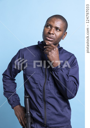 Pensive african american agent contemplating about his responsibility, working on safeguarding a property. Male security guard acting thoughtful, patrol duty in front of camera. Pensive african american agent contemplating about his responsibility, working on safeguarding a property. Male security guard acting thoughtful, patrol duty in front of camera. 124797033