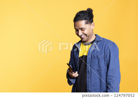 Indian adult chatting with people on remote telephone line in studio, discussing with his friends or close ones against orange background. Young confident joyous man with man bun on a phone call. Indian adult chatting with people on remote telephone line in studio, discussing with his friends or close ones against orange background. Young confident joyous man with man bun on a phone call. 124797052