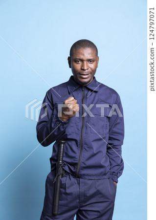 Happy security guard cheering about something in studio, feeling very pleased and enthusiastic in front of camera. Confident bodyguard in uniform with baton showing positivity while on duty. Happy security guard cheering about something in studio, feeling very pleased and enthusiastic in front of camera. Confident bodyguard in uniform with baton showing positivity while on duty. 124797071