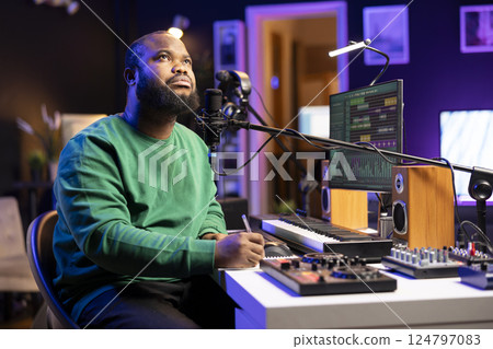 Musician singer thinking about new lyrics to fit into the new song chorus, writing melodic words and rhymes to create a tune in his home studio. Skilled composer making music for an album. Musician singer thinking about new lyrics to fit into the new song chorus, writing melodic words and rhymes to create a tune in his home studio. Skilled composer making music for an album. 124797083