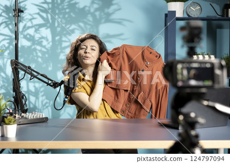 Content creator filming sponsored fashion vlog, unboxing jacket from internet order, mimicking surprise to get subscribers to make purchases from sponsor, doing influencer marketing 124797094