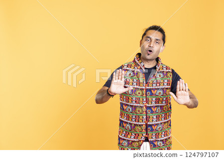 Portrait of stern man doing slow down hand gesture sign, giving advice. Insistent person doing zealous halt sign gesturing, being critical, isolated over studio background 124797107