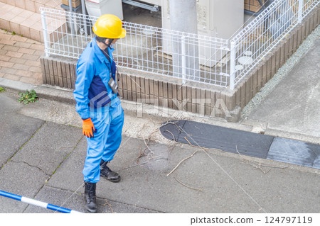 一名維修工人正在從電線桿上的瞭望台上移除掉落的樹枝。 124797119