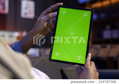 Young remote worker uses green screen on a tablet at his house, feeling carefree in the living room and solving his freelancing tasks. Male person being casual in his apartment, teleworking. 124797166