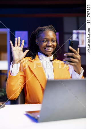 Joyous girl having friendly chat with friends during teleconference meeting using phone. Cheerful teenager doing salute gesturing, having fun catching up with mates during smartphone videocall Joyous girl having friendly chat with friends during teleconference meeting using phone. Cheerful teenager doing salute gesturing, having fun catching up with mates during smartphone videocall 124797173