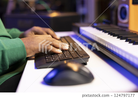 Male artist editing his recorded music in post production, working with a professional software on computer in home studio. Young sound engineer producing tunes for the music industry. Close up. 124797177