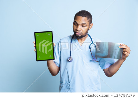 Lively african american nurse pointing to the copy space on tablet and x ray, presenting radiography scan results and diagnosis against blue background. Medical staff in studio. Lively african american nurse pointing to the copy space on tablet and x ray, presenting radiography scan results and diagnosis against blue background. Medical staff in studio. 124797179