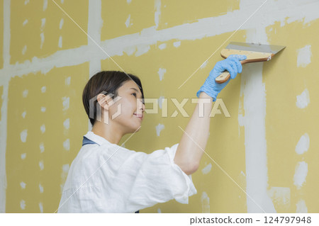 A woman applying putty to plasterboard 124797948