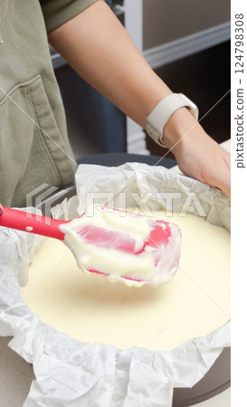 Deliciously Smooth Cake Batter Being Mixed with a Red Spatula in a Black Round Cake Pan 124798308