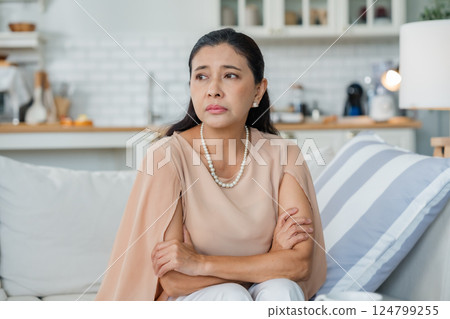 Upset Asian senior woman sitting on sofa, lost in thoughts, feeling lonely Upset Asian senior woman sitting on sofa, lost in thoughts, feeling lonely 124799255