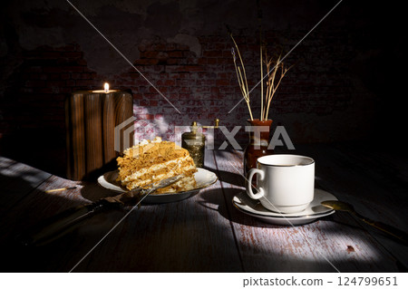 Cup of tea, cake, candle in wooden holder and dried flowers in a ceramic vase casting long shadows Cup of tea, cake, candle in wooden holder and dried flowers in a ceramic vase casting long shadows 124799651