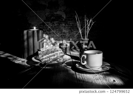 Cup of tea, cake, candle in wooden holder and dried flowers in a ceramic vase casting long shadows 124799652