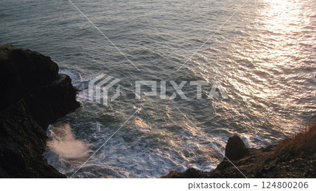 夕陽照射下的海面，白色的海浪拍打著懸崖 124800206