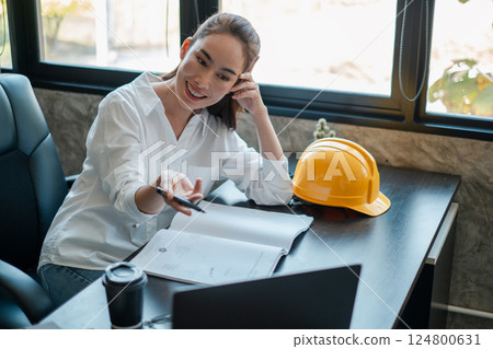 Professional woman architect reviewing project plans in a contemporary office setting, highlighting teamwork and construction industry. 124800631