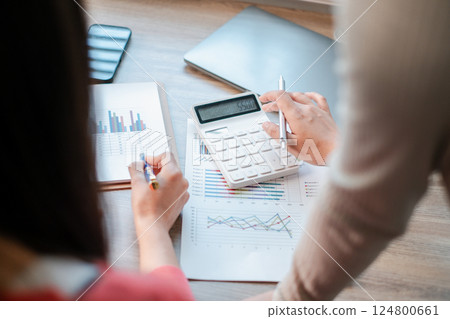 Professionals reviewing financial charts and using a calculator for data analysis in a contemporary office environment. Professionals reviewing financial charts and using a calculator for data analysis in a contemporary office environment. 124800661