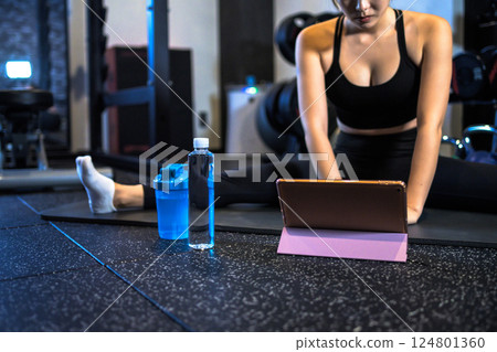 A cool woman stretching at the gym while watching a YouTube video on a tablet How to do it Video viewing 124801360