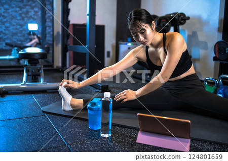 A cool woman stretching at the gym while watching a YouTube video on a tablet How to do it Video viewing A cool woman stretching at the gym while watching a YouTube video on a tablet How to do it Video viewing 124801659