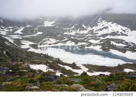 Misty weather in mountains, frozen lake and snow on hillside Misty weather in mountains, frozen lake and snow on hillside 124803089