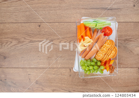 balanced lunch box with fresh fruits, vegetables, meat, and nuts on a wooden background, top view. copy space 124803434