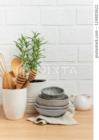 Kitchen utensils, rosemary plant, and ceramic bowls creating a cozy kitchen atmosphere 124803622