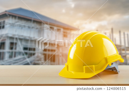 Yellow safety construction helmet on wood table with construction site background 124806515