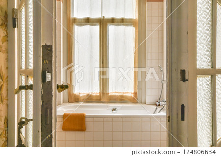 A serene bathroom featuring a bathtub, sunlight streaming through soft curtains, and a cozy atmosphere created by warm colors and textures. 124806634