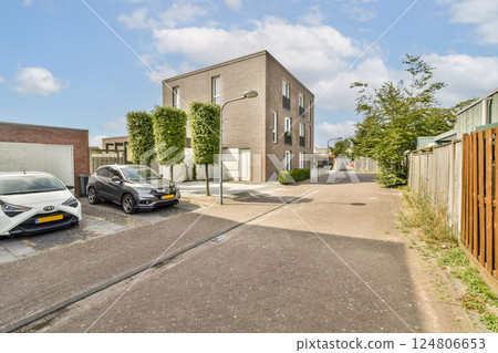 A picturesque view of a modern residential street showcasing contemporary buildings and well-maintained greenery, along with parked cars. 124806653