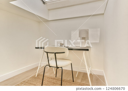 A clean, modern workspace featuring a simple desk, chair, and lamp, enhanced by soft natural light from the skylight above. A clean, modern workspace featuring a simple desk, chair, and lamp, enhanced by soft natural light from the skylight above. 124806670