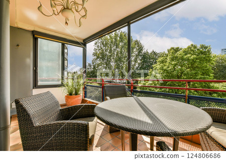 A stylish outdoor balcony featuring comfortable woven furniture, a scenic view of trees, and a bright blue sky, perfect for relaxation and gatherings. 124806686