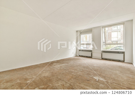 A vacant room featuring two windows allowing ample natural light, highlighting the bare walls and floor. An ideal space for decoration or remodeling. 124806710