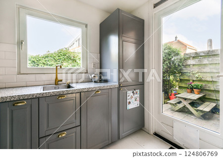 A stylish modern kitchen featuring sleek gray cabinets and a large window showcasing a serene garden view. The space is bright and inviting. 124806769