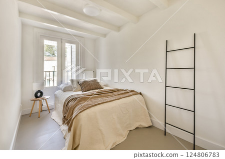 A serene modern bedroom featuring a simple bed with neutral tones, a minimalist aesthetic, and natural light filtering through the window. 124806783