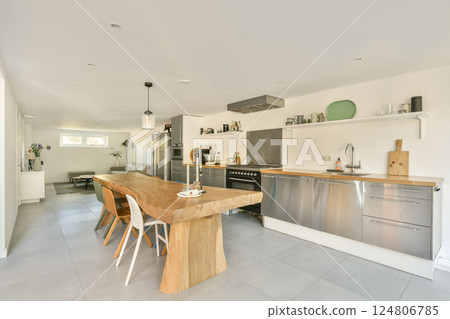 A spacious and contemporary kitchen featuring a wooden dining table, stainless steel appliances, and a sleek design, perfect for modern living. 124806785
