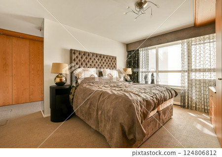 A cozy modern bedroom featuring a large bed, elegant curtains, and stylish furniture, creating a comfortable and inviting atmosphere. 124806812