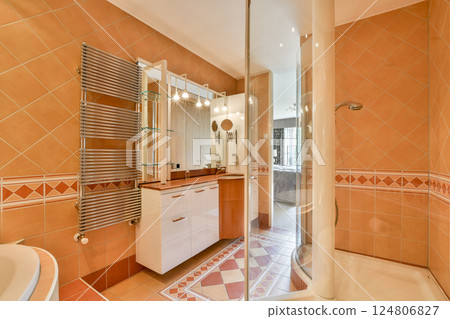 A stylish modern bathroom showcasing elegant design with tiled walls, glass shower, and sleek cabinetry. Bright and inviting ambiance for relaxation. 124806827