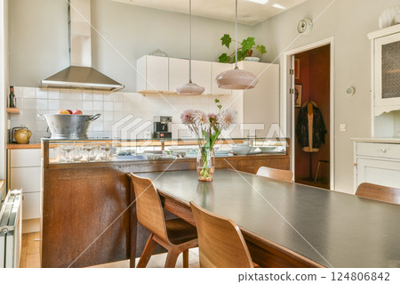 Stylish modern kitchen featuring sleek cabinetry, an elegant dining table, and ample lighting, perfect for family gatherings or culinary creativity. 124806842