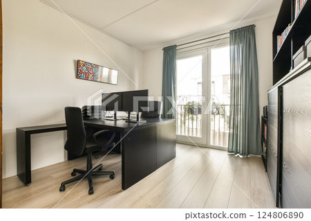 A stylish home office featuring a black desk setup, dual monitors, large windows with curtains, and a warm wooden floor, creating a productive and inviting space. A stylish home office featuring a black desk setup, dual monitors, large windows with curtains, and a warm wooden floor, creating a productive and inviting space. 124806890