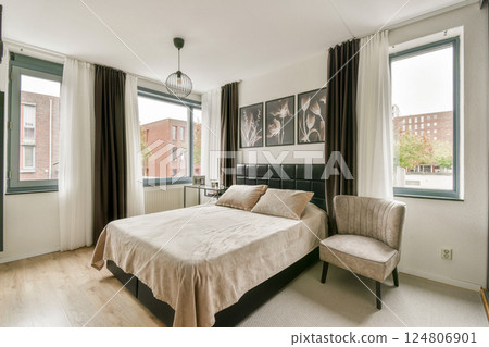 An elegantly designed modern bedroom featuring a stylish bed, contemporary decor, and large windows that bring in natural light. 124806901