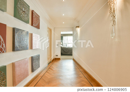 A stylish and sophisticated interior hallway featuring modern artwork on the walls and a polished wooden floor, creating a warm atmosphere. 124806905
