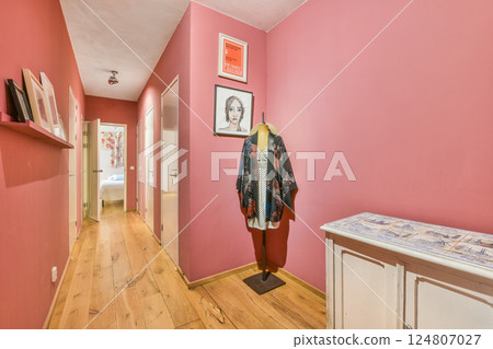 A stylish interior hallway showcases soft pink walls and wooden flooring, accentuated by artwork and strategically placed decorations for an inviting atmosphere. 124807027